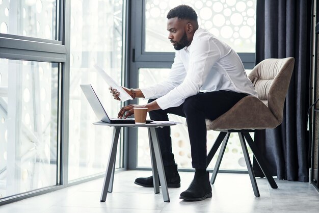 Ansehnlicher afroamerikanischer Geschäftsmann arbeitet am Laptop und analysiert in der speziell benannten