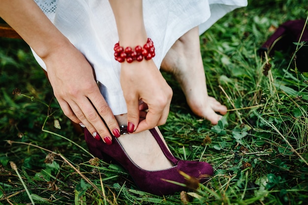 Ansicht der weiblichen Hand zieht Hochzeitsschuhe an. Die Braut bekommt ihre Schuhe im rustikalen Stil. Braut im ukrainischen Stil in bestickten Kleidern.