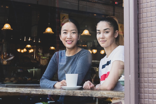 Ansicht durch Fenster der Mama und der Tochter, die im Café mit Kaffeetasse sitzen.