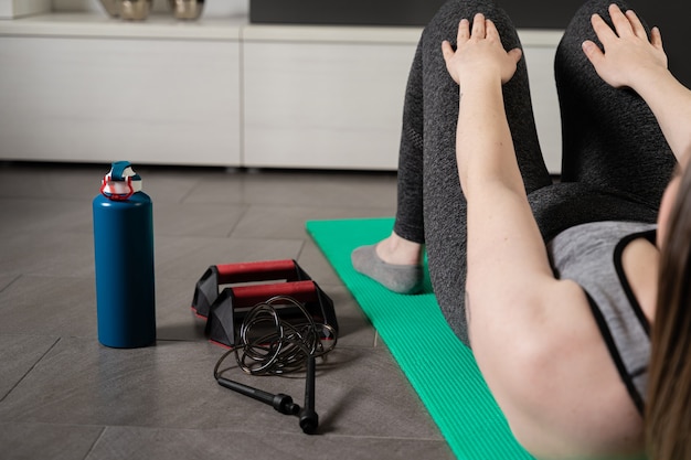 Ansicht einer jungen Frau auf ihrem Rücken, die Sit-ups mit den Sportgeräten neben ihr macht.