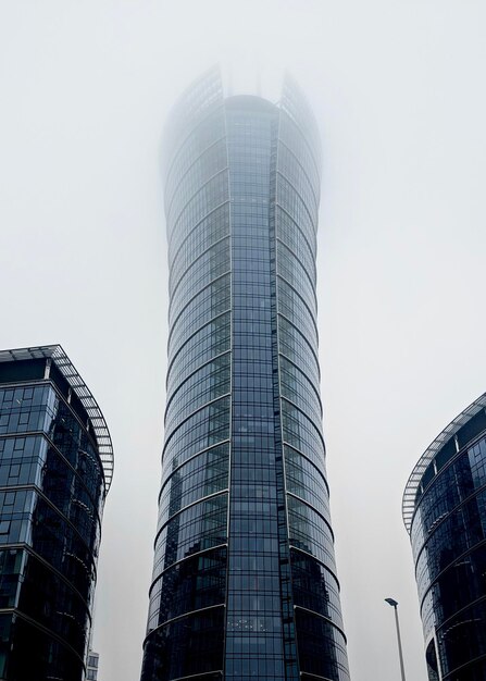 Ansicht eines modernen Geschäftsglaswolkenkratzers unter nebeligem Himmel. Moderne Hochhäuser an einem nassen Regentag