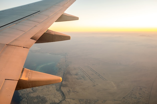 Ansicht vom Flugzeug auf dem weißen Flügel des Flugzeugs, der über Wüstenlandschaft in sonnigem Morgen fliegt.