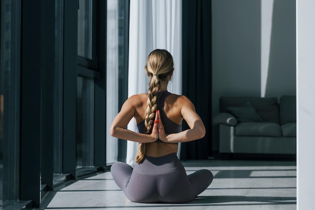 Ansicht von hinten Frau in sportlicher Kleidung, die drinnen Yoga macht