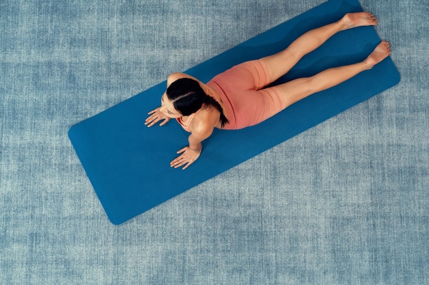 Ansicht von oben: Asiatische Frau in Sportbekleidung macht Yoga-Übungen auf einer Fitnessmatte als Heimtrainingsroutine. Gesunde Körperpflege und ruhige Meditation im Yoga-Lebensstil. Kräftig