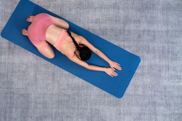 Ansicht von oben: Asiatische Frau in Sportbekleidung macht Yoga-Übungen auf einer Fitnessmatte als Heimtrainingsroutine. Gesunde Körperpflege und ruhige Meditation im Yoga-Lebensstil. Kräftig