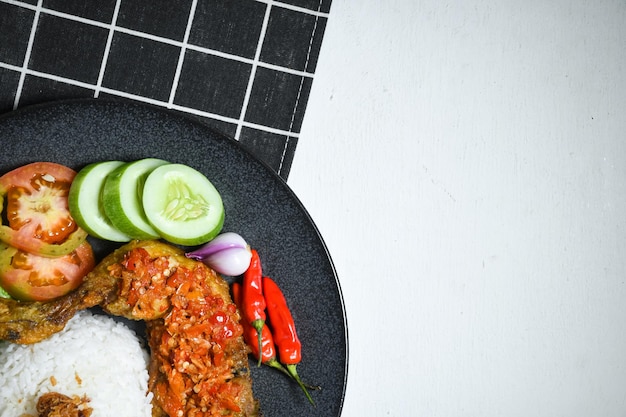 Ansicht von oben Ayam geprek indonesisches Essen mit Sambal Hot Chili Sauce serviert Reis auf schwarzem Teller