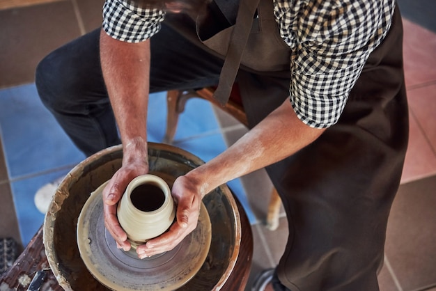 Ansicht von oben. Ceramist verwendet Töpferscheibe und stellt ein handgefertigtes Tonprodukt her.