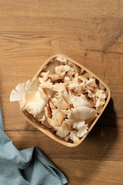 Ansicht von oben Eine Gruppe von weißen Austernpilzen auf Weidenkorb auf braunem Holztisch bereit zum Kochen in der Küche. Platz für Text kopieren