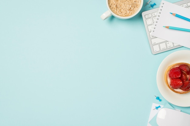 Ansicht von oben Foto des Tastatur-Maus-Organisators blaue Bleistiftstifte Platte mit Erdbeerkuchen und Tasse schaumigem Kaffee auf isoliertem pastellblauem Hintergrund mit Copyspace