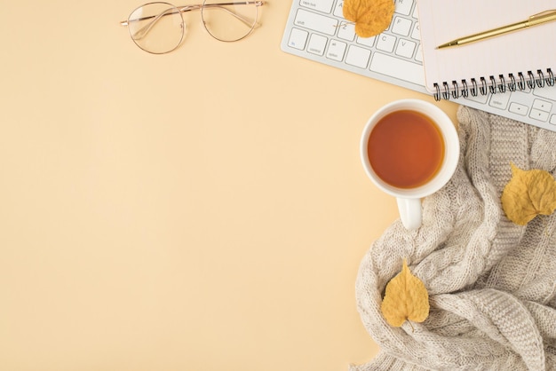 Ansicht von oben Foto von Arbeitsplatz Tastatur Brille goldener Stift Organizer Tasse Tee grauer Schal und gelbe Herbstblätter auf isoliertem beigem Hintergrund mit Copyspace