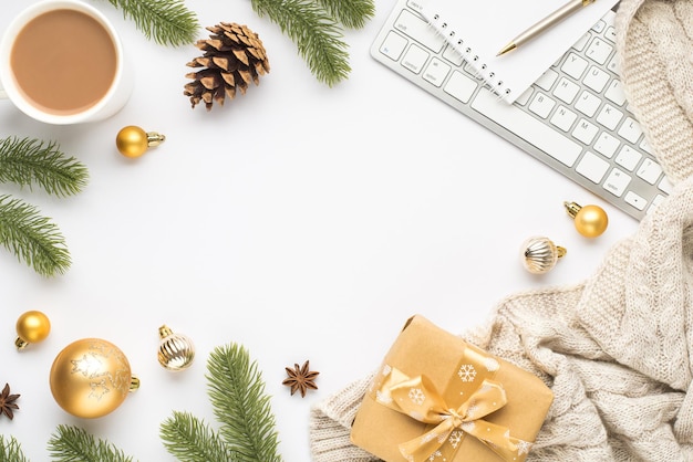 Ansicht von oben Foto von Notebook-Stift-Tastatur-Tasse mit heißen trinkenden Gold-Weihnachtsbaumkugeln, Kiefernzweigen, Kegelanisschal und Geschenkbox auf isoliertem weißem Hintergrund mit leerem Raum in der Mitte