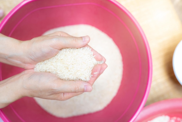 Ansicht von oben Frauenhand, die Reis über einer roten Plastikschüssel hält Globale Lebensmittelkrise Roher Trockenreis Ungekocht