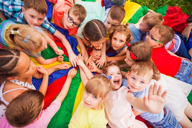 Ansicht von oben Kinder, die Spaß mit auf einer bunten Matte haben, die ihre Hände verbindet Mehrere Kinder, die die Hände hochhalten und lächelnd in die Kamera schauen Kinder im Tagescamp, die versuchen, sich nach aktiven Spielen auszuruhen