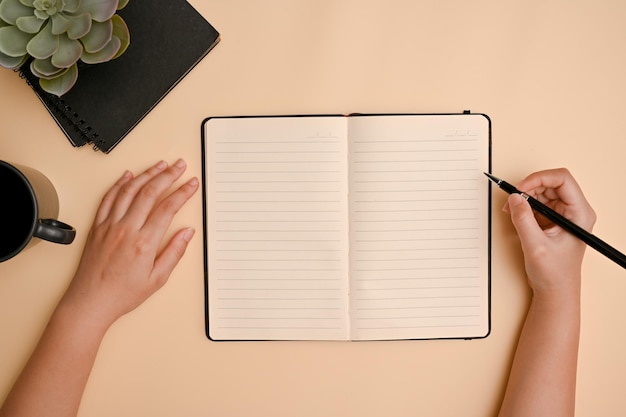 Ansicht von oben Minimale beigefarbene Arbeitsfläche mit weiblicher Handschrift auf ihrem Tagebuch