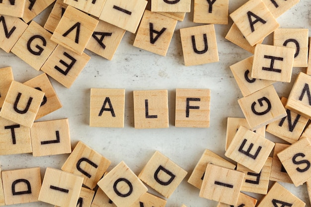 Ansicht von oben nach unten, Stapel quadratischer Holzklötze mit Buchstaben ALF (steht für Always listen first) auf Whiteboard.