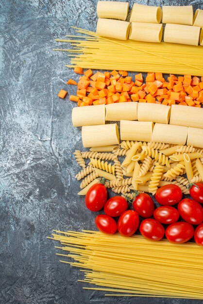 Ansicht von oben verschiedene Pasta Penne Rigatoni Spaghetti Spiralen Kirschtomaten gehackte Karotte auf grauem Hintergrund