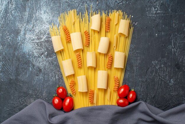 Ansicht von oben verschiedene Pasta Rigatoni Spaghetti Spiralen Kirschtomaten lila Schal auf grauem Hintergrund