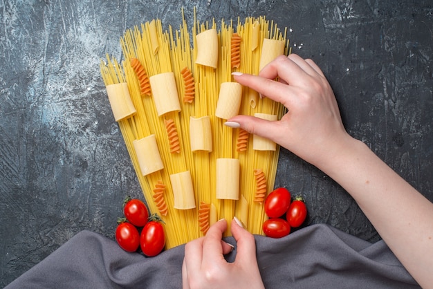 Ansicht von oben verschiedene Pasta Rigatoni Spaghetti Spiralen Kirschtomaten lila Schal weibliche Hände halten Pasta auf grauem Hintergrund