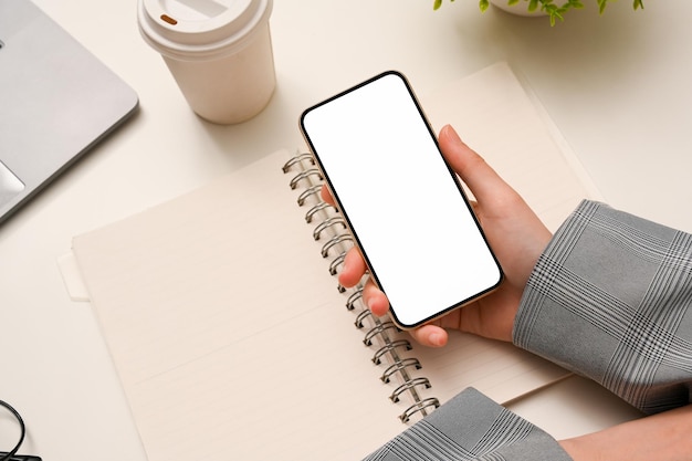 Ansicht von oben Weibliche Hände, die einen leeren leeren Bildschirm des Smartphones über ihrem minimalen weißen Schreibtisch halten