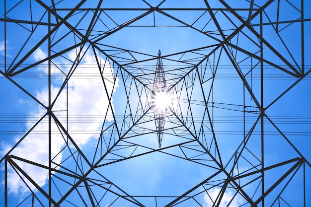 Ansicht von unten des Hochspannungsturms und der Stromleitungen gegen Wolke auf blauem Himmelshintergrund an sonnigen Tagen