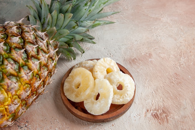 Ansicht von unten frische Ananas trockene Ananasringe auf Holzplatte auf beigem Tisch