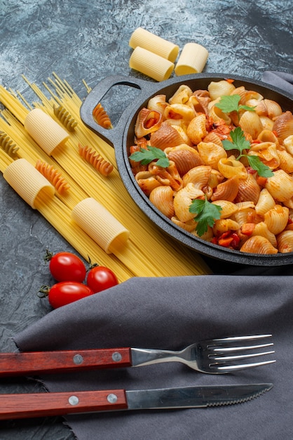 Ansicht von unten leckere Pasta in Bratpfanne Spaghetti Rigatoni Spiralen Gabel und Messer auf grauem Hintergrund