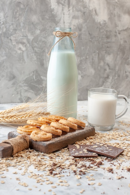 Ansicht von unten verschiedene Kekse auf Schneidebrett Pralinen Weizenspitzen Milchflasche Tasse Milch Hafer auf dem Tisch verstreut