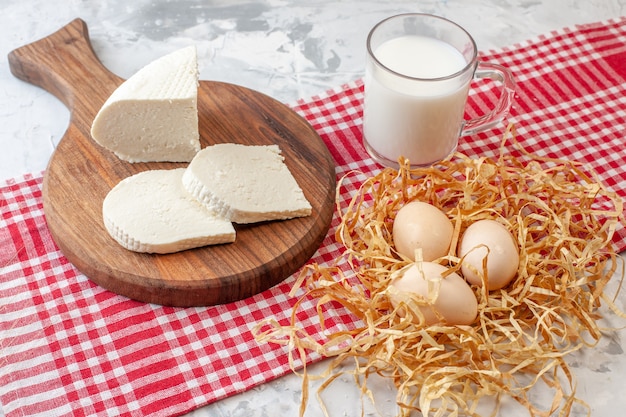 Ansicht von unten weiße Käsescheiben auf Schneidebrett Hühnereier auf Stroh Tasse Milch rot weiß karierte Tischdecke auf Tisch