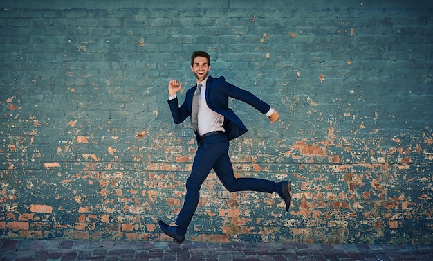 Ansioso por tener éxito Retrato de un joven empresario corporativo saltando en el aire contra una pared de ladrillos