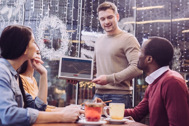 Ansprechend befriedigte vier Kollegen, die Zeit im Café verbringen, während Mann unten schaut und Laptop hält