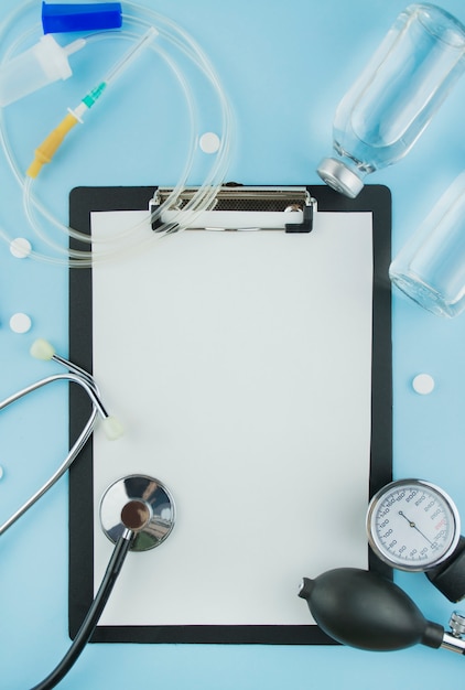 Antecedentes médicos Libro blanco en el portapapeles con pluma, estetoscopio, sistema cuentagotas, solución sobre un fondo azul. La medicina. Copia espacio Endecha plana.