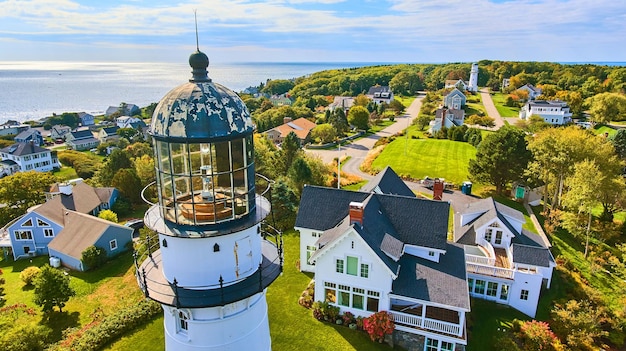 Antena de cerca en la parte superior del faro blanco con casas y vista al mar en Maine