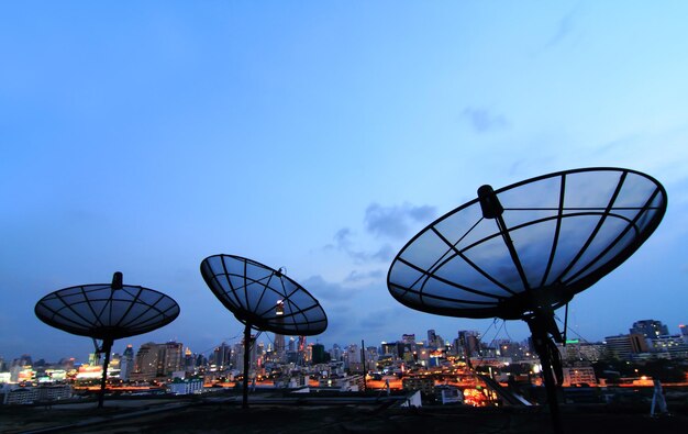 Foto antena negra de comunicación por satélite sobre el cielo al atardecer en el paisaje urbano