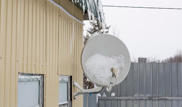 Antena parabólica fixada na parede de uma casa na neve após uma queda de neve