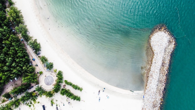 Foto antenne des wellenbrechers der strand mit blick auf eine gruppe von menschen und kleines fischerboot auf weißem sandstrand, bäumen und klarem meerwasser.