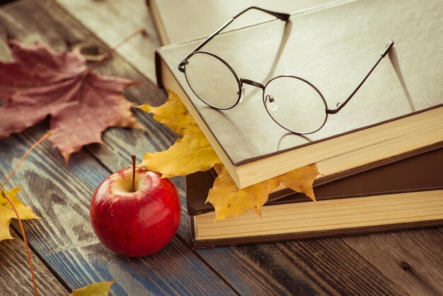Anteojos con libro y hojas de otoño en la mesa