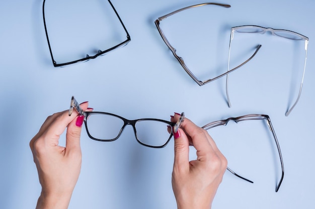 Anteojos en mano femenina sobre fondo azul Prueba de visión de tienda óptica concepto de gafas elegantes