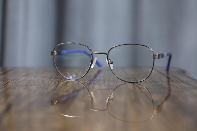 anteojos sobre una mesa de madera con cortinas azules en el fondo