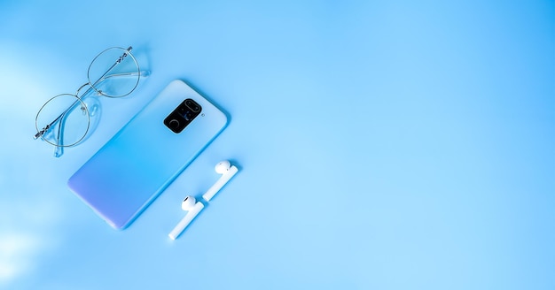 anteojos de teléfono y auriculares en un lugar de banner de fondo azul para el texto de los aparatos del hombre moderno