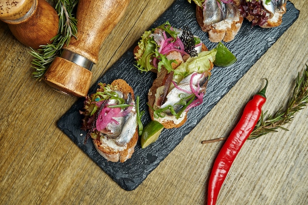 Antepasto - brusqueta com espadilha salgada luz ou arenque, queijo feta em uma baguete francesa em uma bandeja de pedra. Vista superior, plana leigos com espaço de cópia