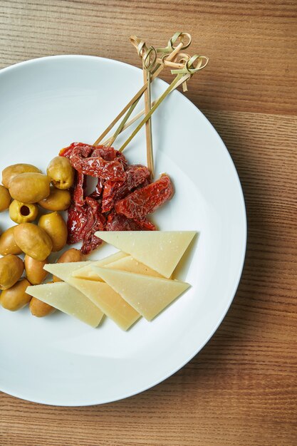 Antepasto italiano apetitoso - tomates secos ao sol, azeitonas e parmesão em um prato branco sobre uma mesa de madeira