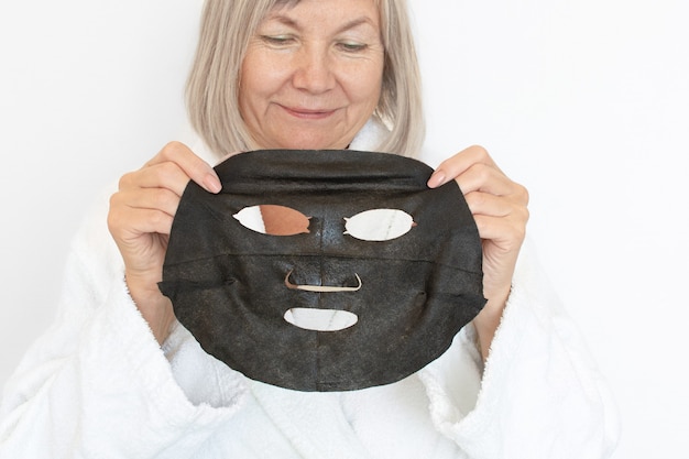 Foto anti-age-konzept. ältere frau trägt eine schwarze kosmetische maske auf ihr gesicht auf.