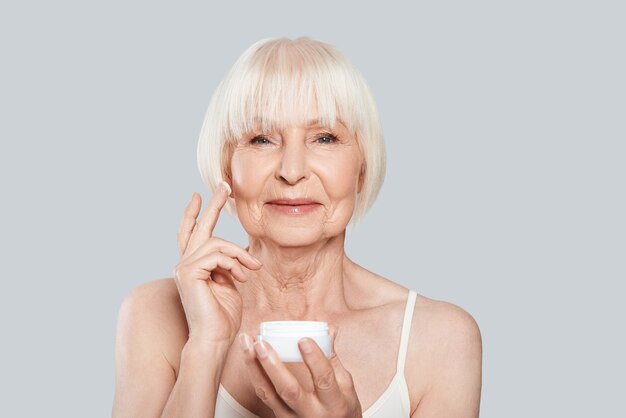 Anti-envelhecimento. Linda mulher sênior aplicando produtos de beleza