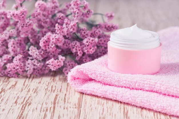 Anti-Falten-Anti-Aging-Creme-Körperpflege oder Gesichtspflege-Hygiene-Feuchtigkeitslotion mit rosa Blüten in Plastikglas mit Handtuch auf Holztisch.