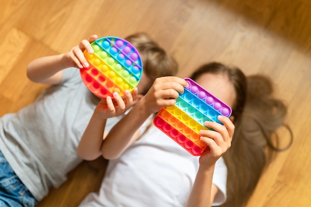 Anti-Stress-sensorisches Pop-it-Spielzeug in Kinderhänden. Ein kleines glückliches Kind spielt zu Hause mit einem einfachen Grübchenspielzeug. Kleinkinder halten und spielen Popit Rainbow Farbton helle Farbe, Trend 2021 Jahr