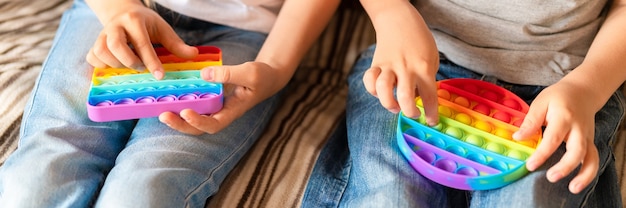 Anti-Stress-sensorisches Pop-it-Spielzeug in Kinderhänden. Ein kleines glückliches Kind spielt zu Hause mit einem einfachen Grübchenspielzeug.