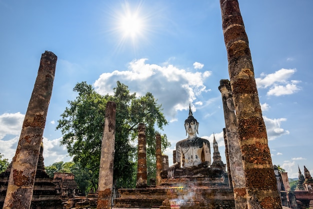 Antiga estátua do Buda sentada entre as ruínas sob o sol forte de Wat Maha. Esse templo no Parque Histórico de Sukhothai é uma cidade antiga e famosa atração turística da província de Sukhothai, Tailândia