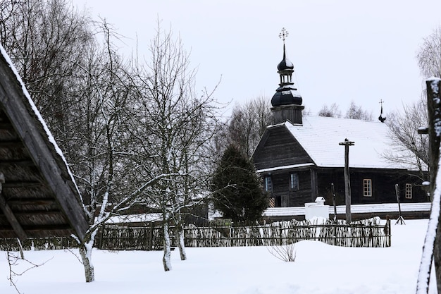 Antiga igreja de madeira feita de troncos redondos cruz na cúpula paisagem russa de inverno árvores cobertas de neve antiga vila russa abandonada coberta de neve