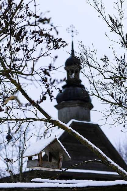 Antiga igreja de madeira feita de troncos redondos Cruz na cúpula Paisagem russa de inverno Árvores cobertas de neve Antiga vila russa abandonada coberta de neve