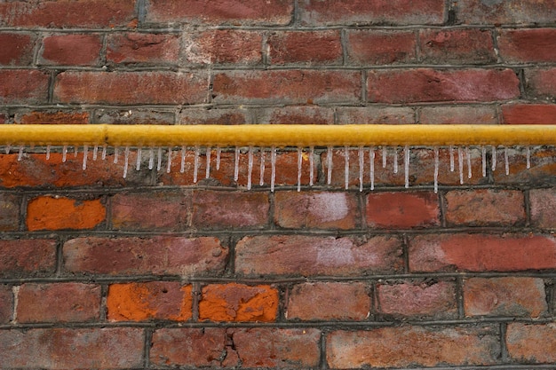 Antiga muralha de tijolos com um tubo amarelo com pingentes de gelo na cidade de inverno